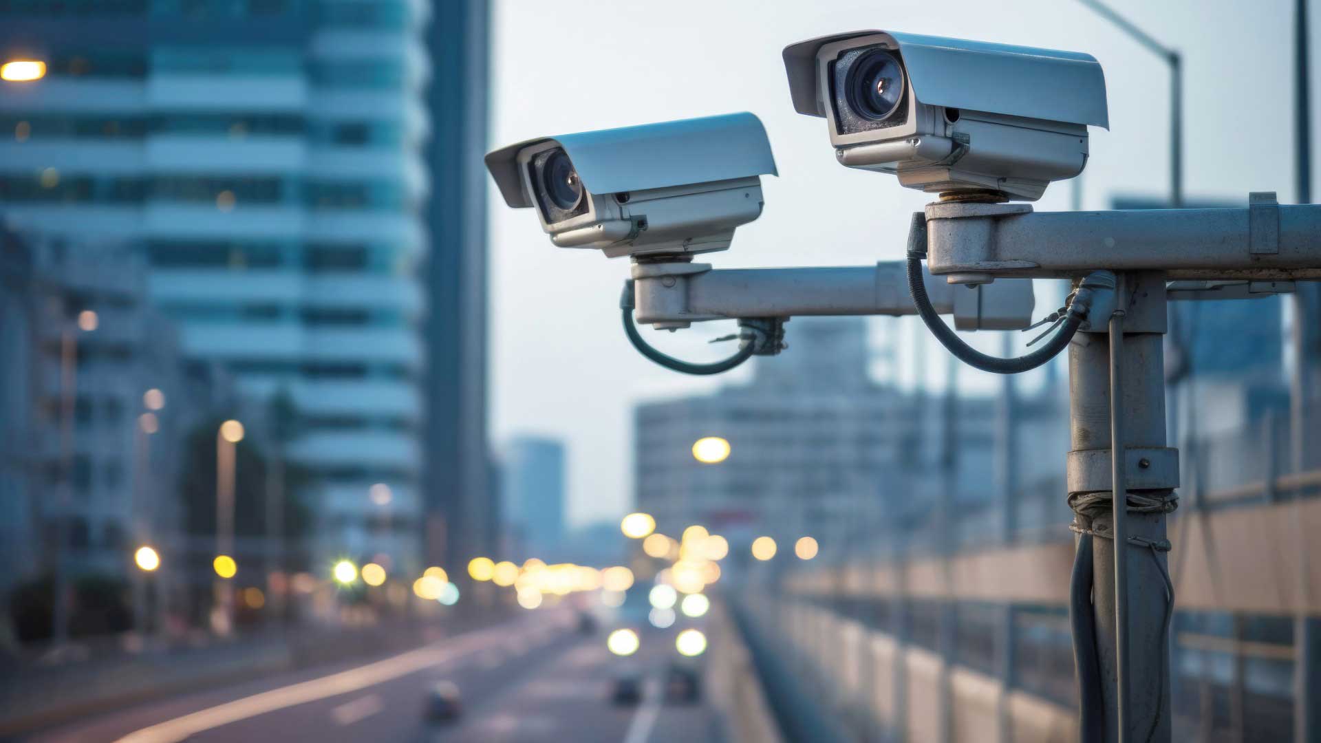 Zwei Überwachungskameras im urbanen öffentlichen Raum mit einer belebten Straße im Hintergrund, symbolisiert Videoüberwachung zu Sicherheitszwecken