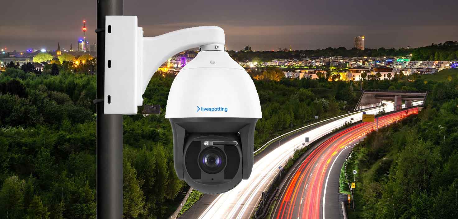Eine weiße livespotting PTZ-Kamera, montiert an einem Mast, vor dem Hintergrund einer nächtlichen Autobahn mit den leuchtenden Lichtspuren des fließenden Verkehrs. Das Bild symbolisiert den Einsatz von Live-Webcams zur Analyse von Verkehrsströmen und zur Lagebeurteilung in Städten.